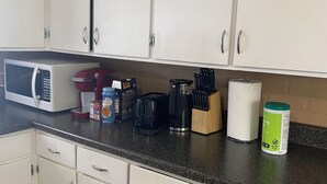 Een keuken met witte kastjes, een magnetron, een koffiezetapparaat en diverse keukenbenodigdheden op het aanrecht.