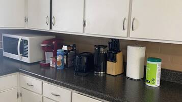 Ett kök med vita skåp, en mikrovågsugn, en kaffebryggare och diverse köksredskap på bänkskivan.