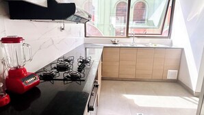 A modern kitchen with a gas stove, a red blender, and a window overlooking a street. - Charming 3-bedroom high-rise condo in the safest downtown neighborhood (La Paz)