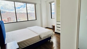 A bedroom with a bed, a desk, and a view of a cityscape through large windows. - Charming 3-bedroom high-rise condo in the safest downtown neighborhood (La Paz)