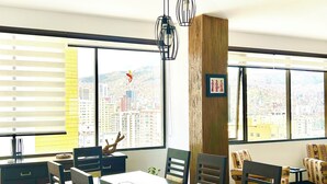 A modern dining area with a large table, chairs, and a city view through large windows. - Charming 3-bedroom high-rise condo in the safest downtown neighborhood (La Paz)