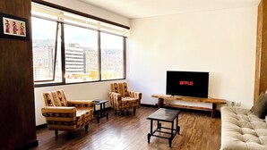 A living room with a large window, a TV on a wooden stand, and two patterned armchairs. - Charming 3-bedroom high-rise condo in the safest downtown neighborhood (La Paz)