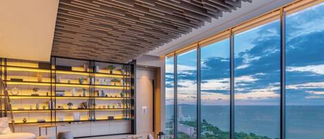 A modern interior with a large window overlooking a coastal view, a built-in bookshelf, and a seating area.