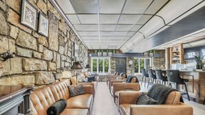 Un espace intérieur vaste, avec un mur en pierre, des canapés en cuir et un coin bar.