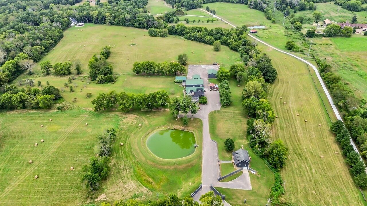 Ein Luftbild eines Grundstücks mit einem großen grünen Feld, einem Teich und einem Gebäude mit einer grünen Dachbegrünung.
