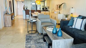 Un salon moderne avec un canapé gris, une table basse en bois et un vase bleu. On aperçoit à l’arrière-plan un coin repas avec une table et des chaises en bois.