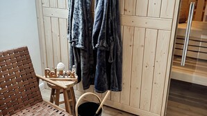 A wooden sauna room with towels hanging on hooks, a wooden chair, a small table with a cup and a candle, and a sauna control panel. - Bachgeflüster suite, incl. whirlpool, sauna (Bad Kötzting)