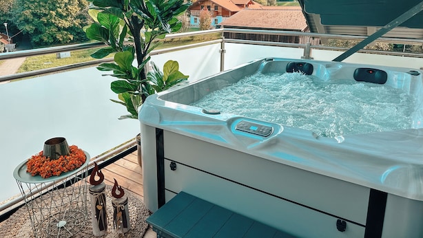 A hot tub with a view of a lake and a house in the background. - Bachgeflüster suite, incl. whirlpool, sauna (Bad Kötzting)