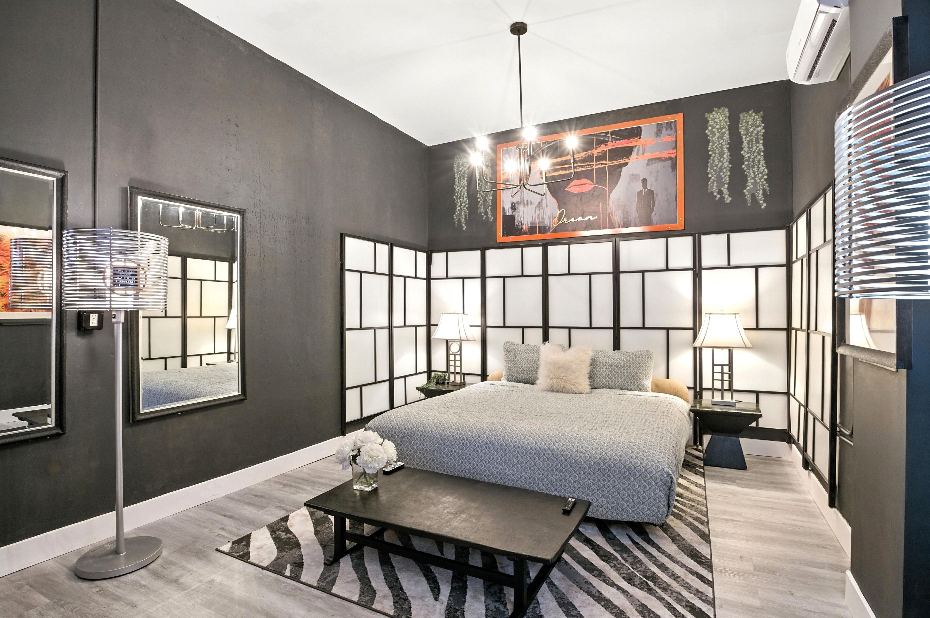 Een moderne slaapkamer met een groot bed, nachtkastjes met lampen, een staande lamp en een lijst met een afbeelding aan de muur.