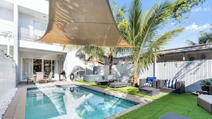 Una piscina amb una tanca blanca, mobles d'exterior i una palmera.