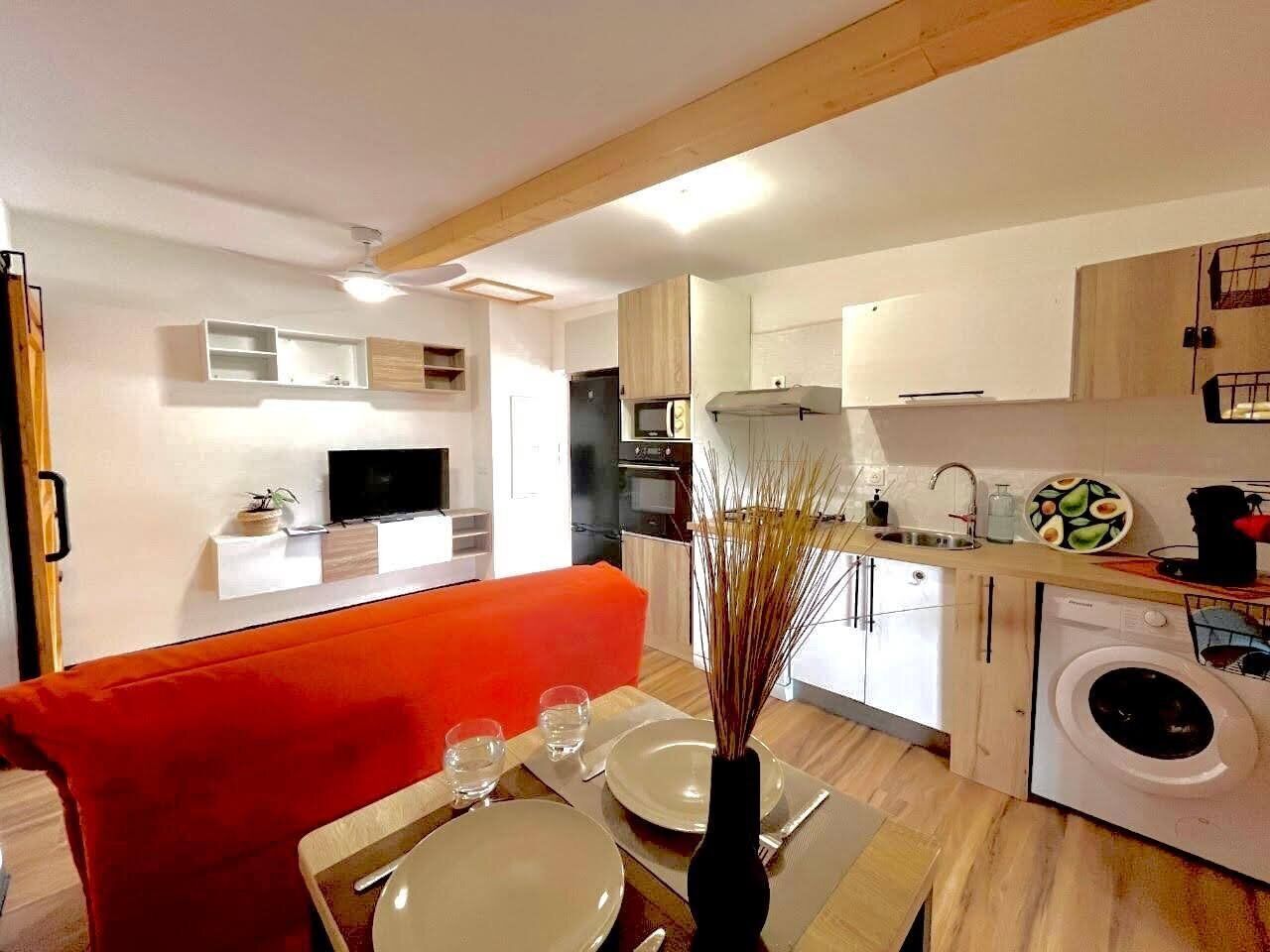 Une cuisine moderne avec des meubles blancs, un lave-linge et un coin repas comprenant un canapé rouge et une table dressée pour deux personnes.