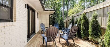 A wooden deck with Adirondack chairs, a small table, and a brick wall.