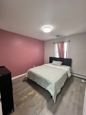 Et soveværelse med seng, natbord, et vindue med gardiner og en loftlampe.
