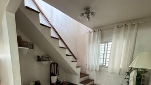 A spacious living area with a staircase, a ceiling fan, and a window with curtains.