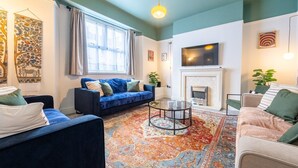 A living room with a blue sofa, a round coffee table, and a fireplace. - Emerald House by Tŷ SA (Newport)