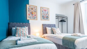 A hotel room with two beds, a wardrobe, and two framed floral artworks on the wall. - Emerald House by Tŷ SA (Newport)