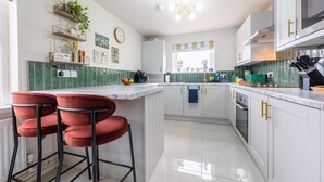 A modern kitchen with white cabinets, a marble countertop, and a central island with red bar stools. - Emerald House by Tŷ SA (Newport)