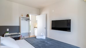 Una habitación de hotel moderna con cama, televisor montado en la pared, vestidor y baño visible a través de una puerta abierta.