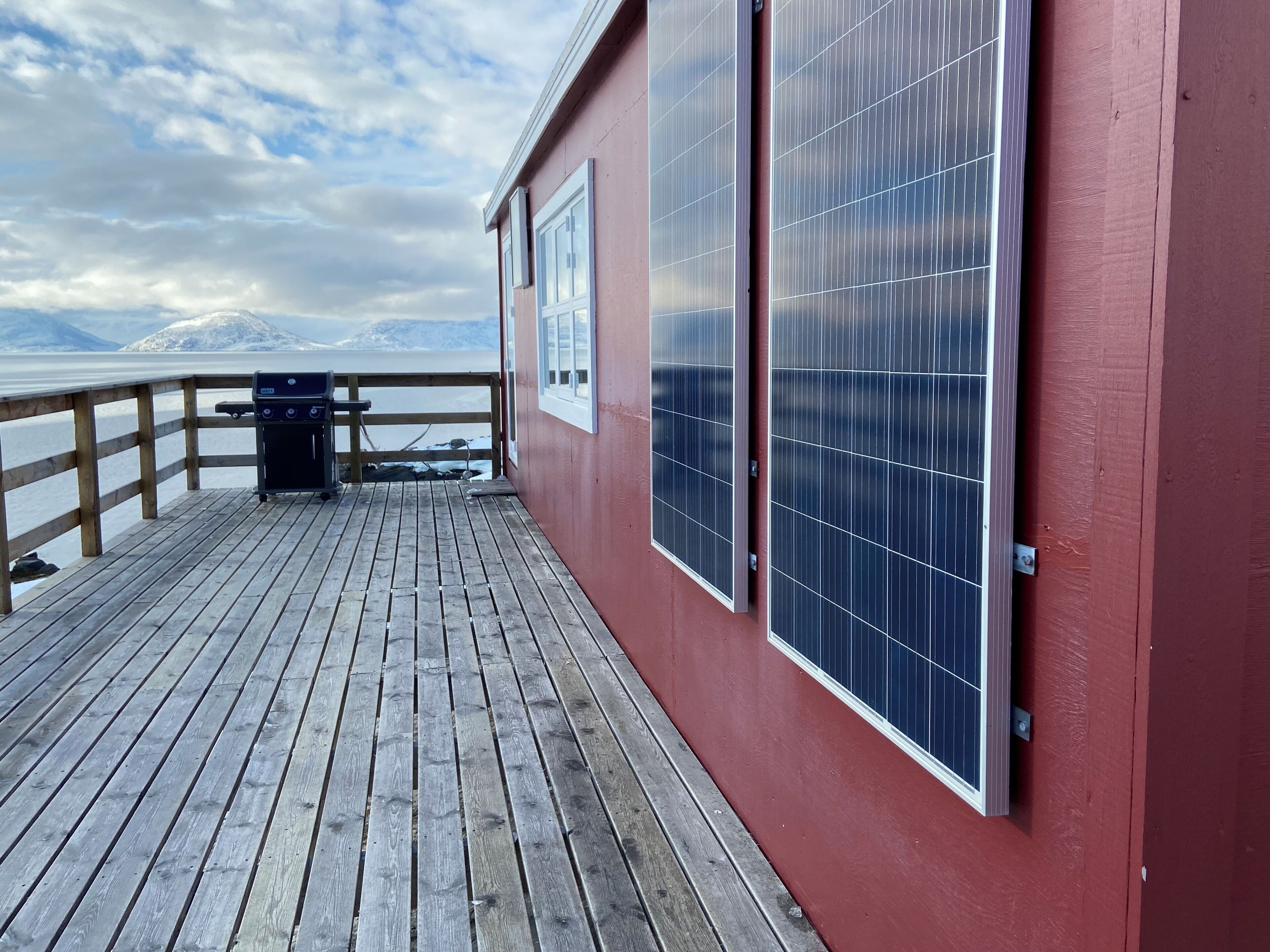Una terraza de madera con paneles solares, una parrilla y vistas a la montaña.