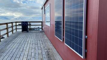 Una terraza de madera con paneles solares, una parrilla y vistas a la montaña.