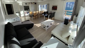 Una sala de estar moderna con un sofá, una mesa de comedor con sillas y vista al mar a través de amplios ventanales.