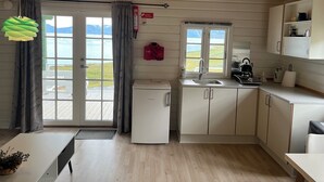 Cocina compacta con refrigerador, lavamanos y armarios, ventana con vistas al exterior y puerta que da a un balcón.