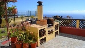 Eine Terrassenanlage im Freien mit einem Ziegel-Barbecue, Kübelpflanzen und Blick aufs Meer.