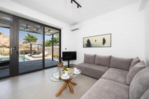 Ein modernes Wohnzimmer mit einem Glastisch, einem grauen Sofa und einem Fernseher.