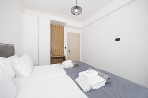A modern hotel room with a large bed, a wooden wardrobe, and a small seating area with towels.