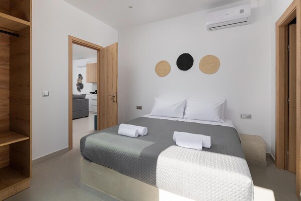 Une chambre moderne avec un lit, deux tables de chevet, une armoire et une salle de bain visible à travers une porte ouverte.