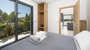 Une chambre moderne dotée d’une grande porte-fenêtre coulissante, d’un lit avec une literie grise, d’une étagère intégrée en bois et offrant une vue sur l’extérieur.