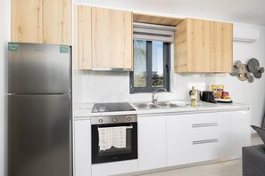 Une cuisine moderne dotée d’appareils électroménagers en acier inoxydable, de meubles en bois, d’une fenêtre et d’un plan de travail sur lequel se trouvent une bouteille et des en-cas.