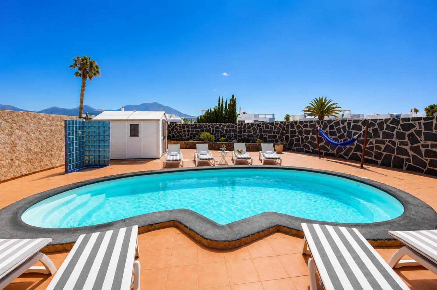 A swimming pool with lounge chairs, a stone wall, and a mountain in the background.