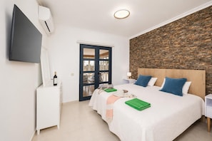 A hotel room with a bed, a TV, an air conditioner, a wooden headboard, and a stone wall.