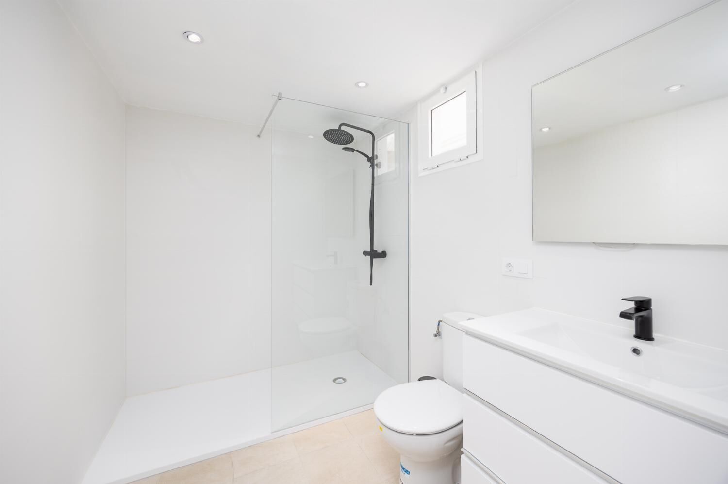 Un baño moderno con cabina de ducha de vidrio, un inodoro blanco y un lavamanos con espejo.