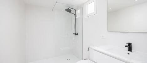 Un baño moderno con cabina de ducha de vidrio, un inodoro blanco y un lavamanos con espejo.