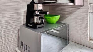 A compact kitchen with a built-in coffee maker, a green colander, and stacked white plates on a wooden shelf. - Nice, cozy room in Escandon CDMX (Ciudad de México)