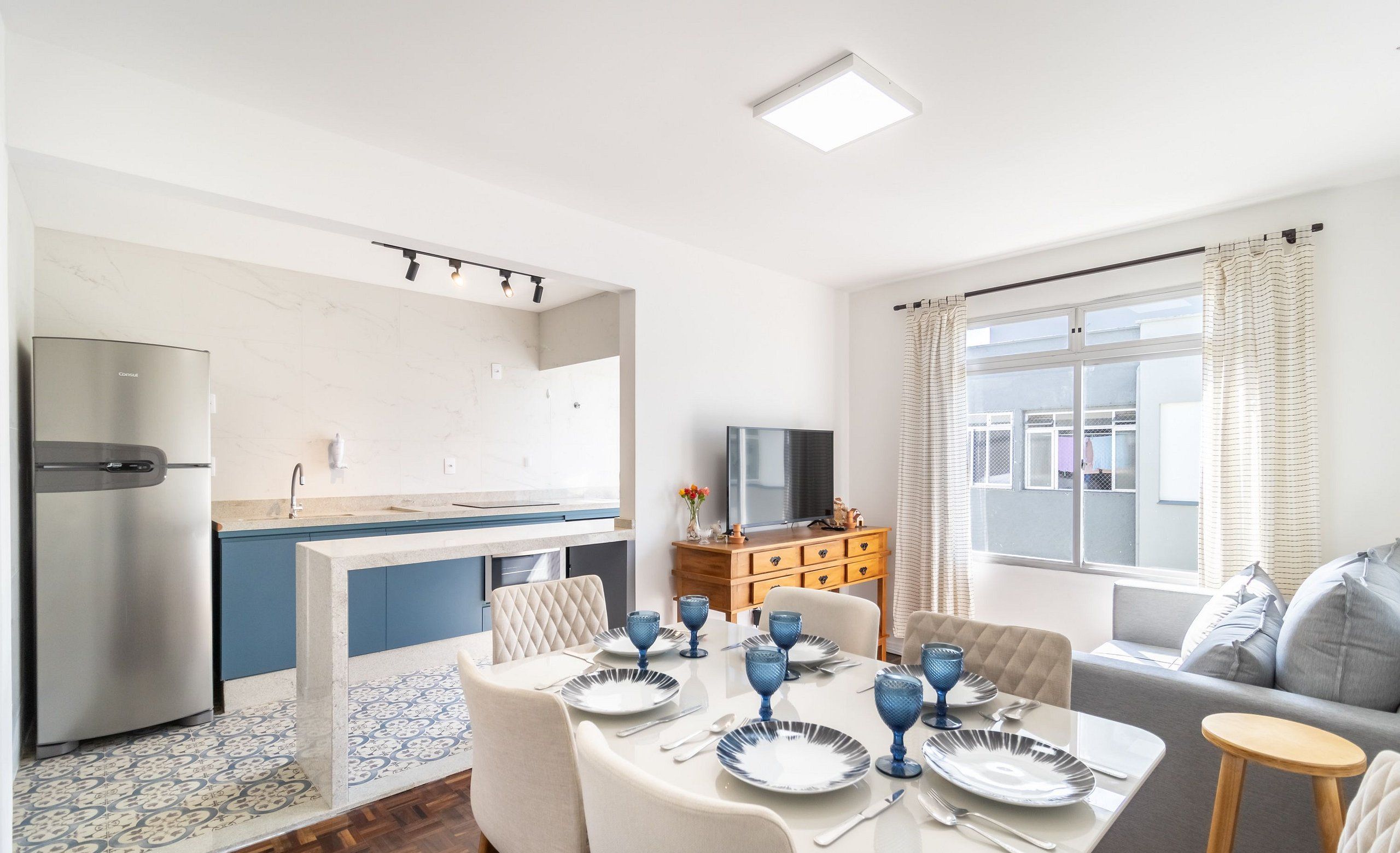 A modern kitchen with a built-in fridge, a dining area with a table set for four, and a sofa in the living area.
