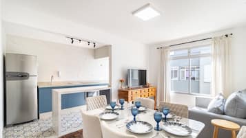 A modern kitchen with a built-in fridge, a dining area with a table set for four, and a sofa in the living area.