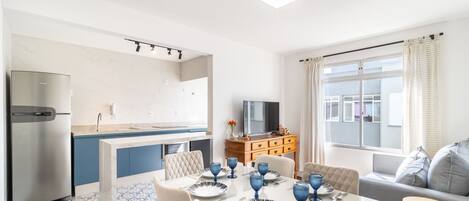 A modern kitchen with a built-in fridge, a dining area with a table set for four, and a sofa in the living area.