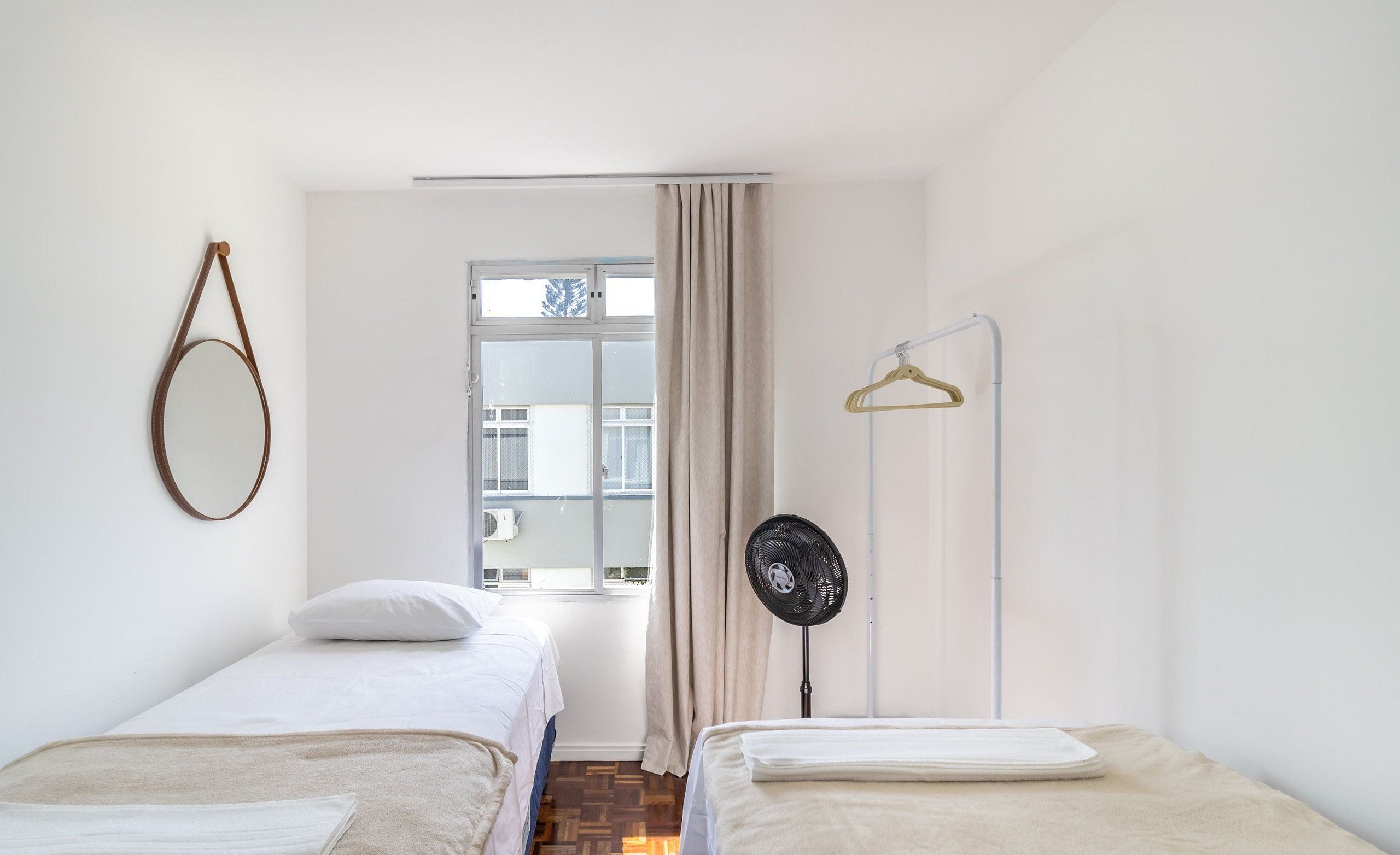 Een kamer met twee bedden, een spiegel aan de muur, een ventilator en een raam met gordijnen.
