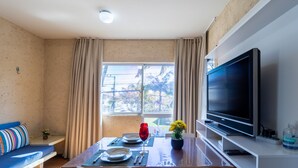 A modern room with a dining table, chairs, a sofa, a TV, and a window with curtains. - Apt 6 min From the sea in Canasvieiras-sc Rba201 (Florianópolis)