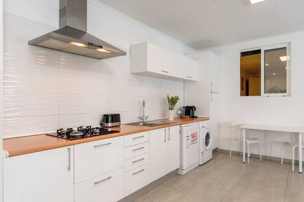 A modern kitchen with white cabinets, a stainless steel range hood, a gas stove, a washing machine, and a dining area with a table and chairs.