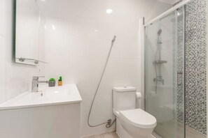 A modern bathroom with a white sink, toilet, and glass shower enclosure.