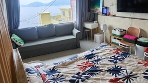 Ett hotellrum med en säng, ett skrivbord, en tv och utsikt över havet.