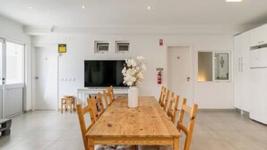 Zona de menjador moderna amb taula i caires de fusta, televisió i un ram de flors.