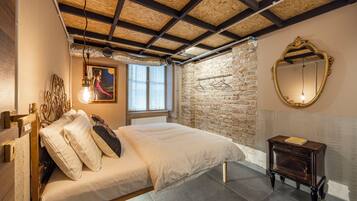 A bedroom with a bed, a wooden headboard, a brick wall, a window, and a mirror.