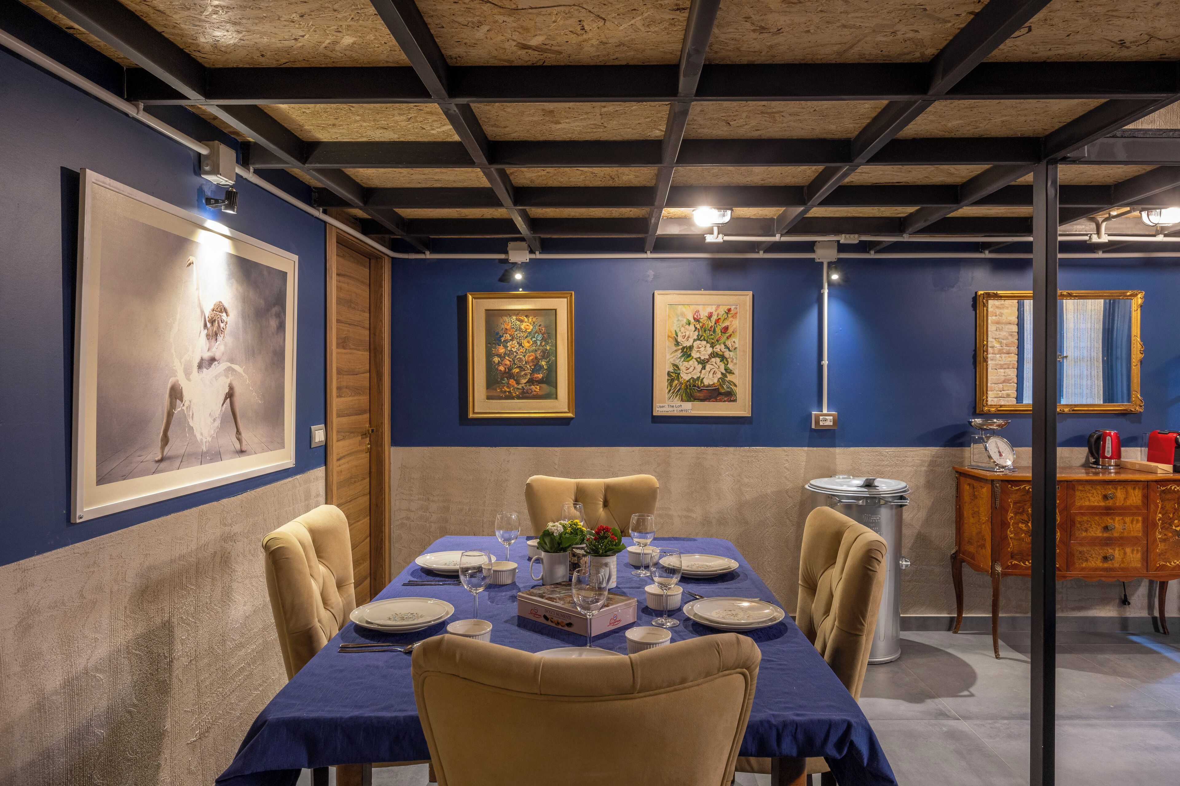 A dining room with a long table set for six, framed artwork on the walls, and a vintage-style cabinet in the background.