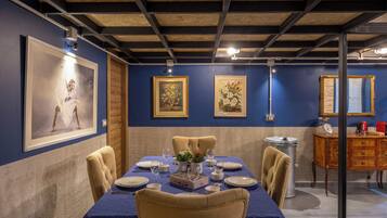 A dining room with a long table set for six, framed artwork on the walls, and a vintage-style cabinet in the background.