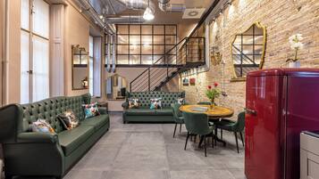 A cozy living room with a green sofa, a dining table with chairs, a red refrigerator, and a brick wall.
